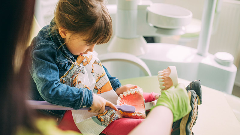 Mädchen lernt beim ersten Besuch beim Kinderzahnarzt, wie man sich die Zähne putzt.